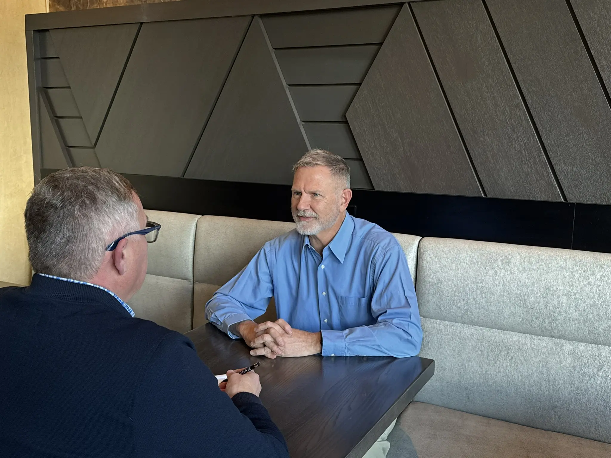 Two men engaged in a conversation at a modern restaurant booth.