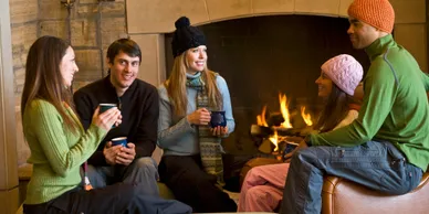 Friends enjoying drinks by a cozy fireplace in winter attire.